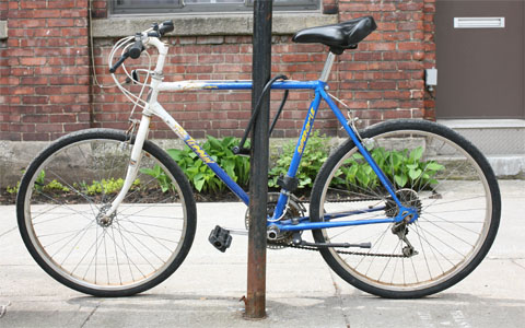 blue and white male bike locked on a pole with house in the background
