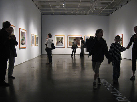 gallery space with visitors looking at photographs on the three walls
