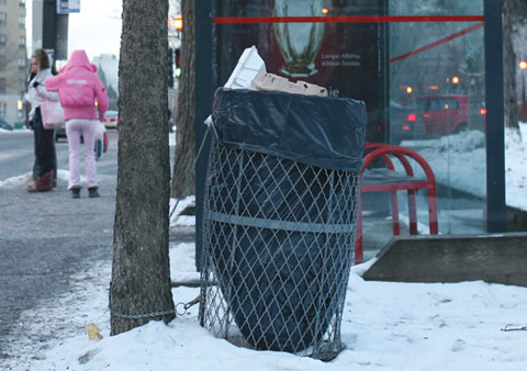 Garbage can on Rue Sherbrooke E, Corner Avenue Emile-Duploye with a busstop and people waiting