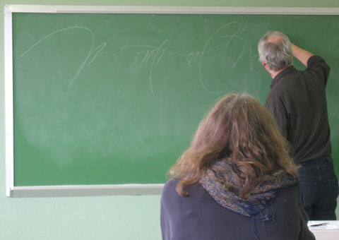 Calligrapher writing on green chalkboard in classroom